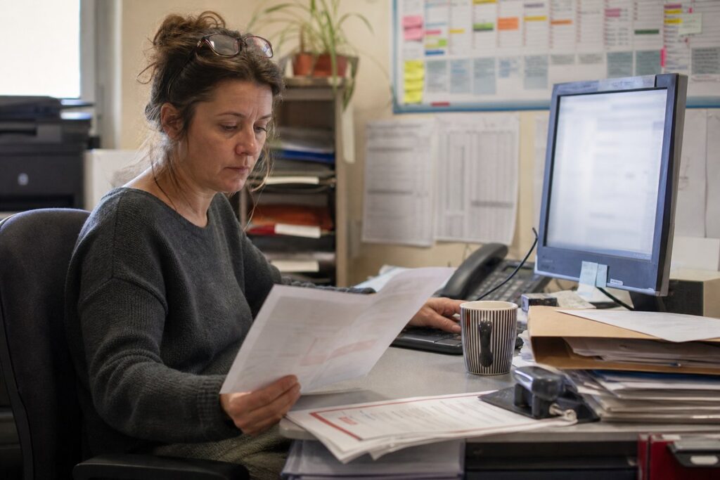Assistante traitant les documents administratifs d'une TPE française à son poste de travail